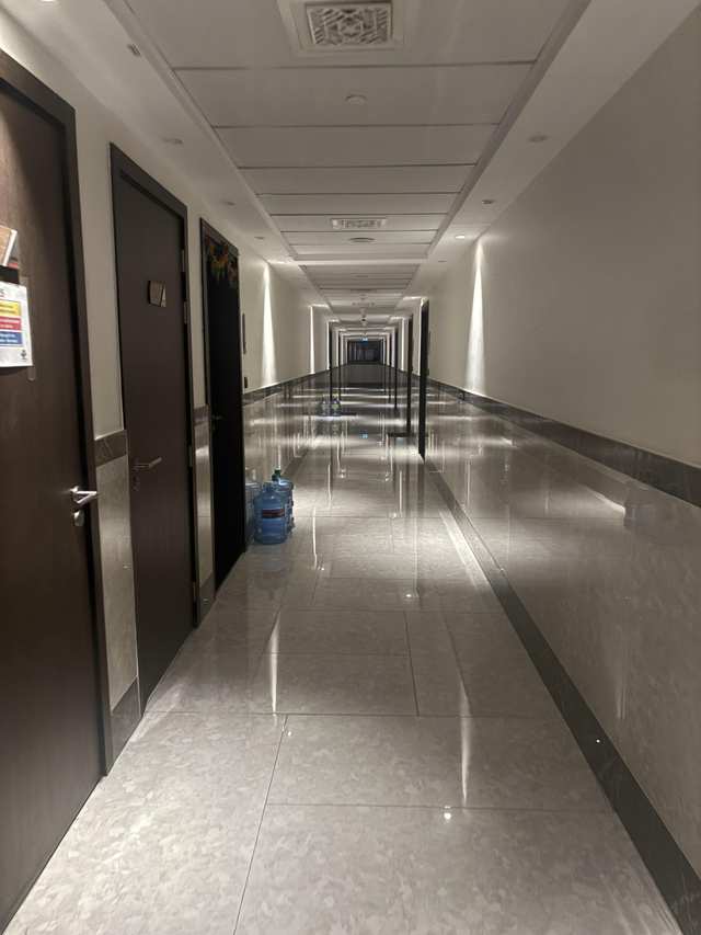 A long empty hallway with dark doors, glossy tiles, reflective wall panels, and water bottles.