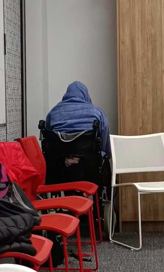 A covered CPR mannequin sits facing a corner behind stacked chairs.