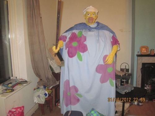 A person-sized flower costume hangs in a cramped domestic room.