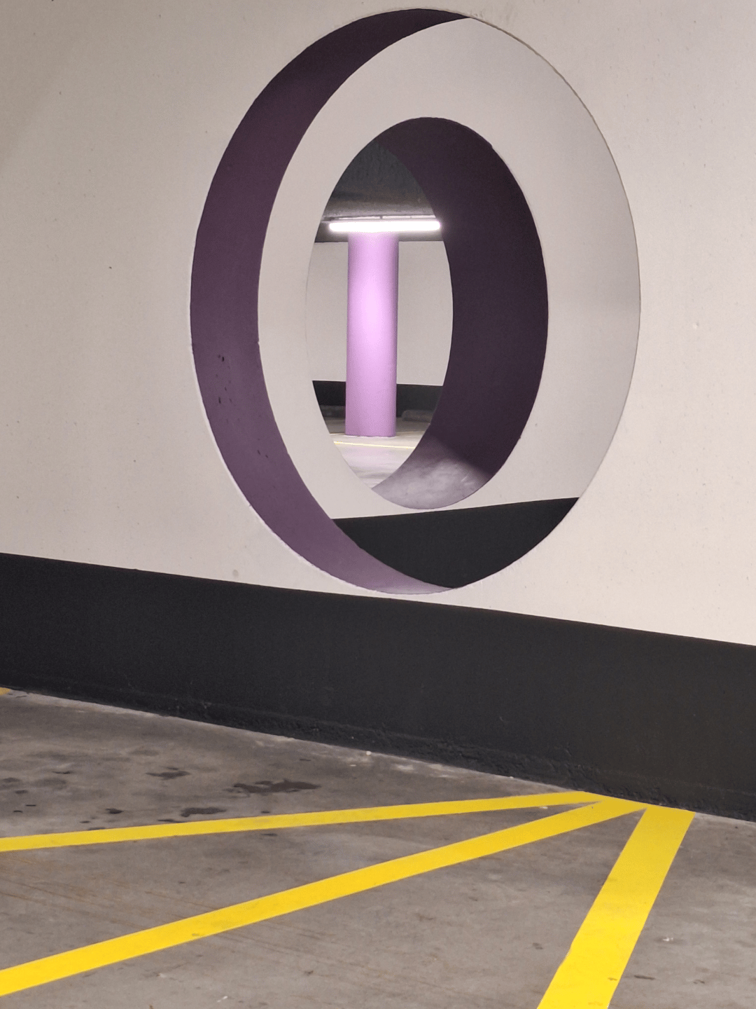Two round openings aligned through parking-garage walls, with a purple column visible through both.