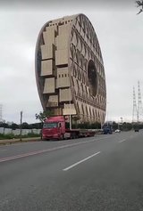 A flatbed truck parked in front of an oval building appears to be carrying the building.
