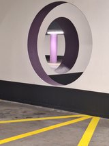 Two round openings aligned through parking-garage walls, with a purple column visible through both.