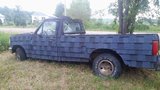 A parked pickup truck has blue asphalt roofing shingles attached across its hood, doors, and bed.