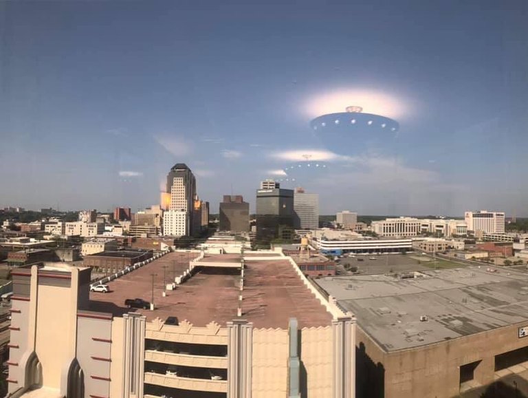 Ceiling lights reflected in a window appear as bright objects above a city in daylight.